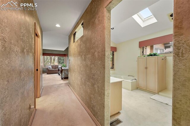hall featuring visible vents, a skylight, light carpet, and high vaulted ceiling