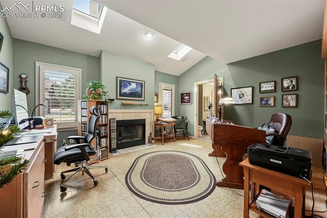 office area featuring a tiled fireplace, vaulted ceiling with skylight, and plenty of natural light