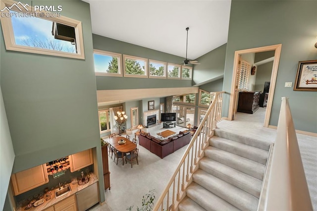 staircase with high vaulted ceiling, a ceiling fan, carpet, and a fireplace with raised hearth
