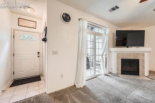 carpeted foyer entrance featuring tile patterned flooring, a ceiling fan, baseboards, a tile fireplace, and visible vents