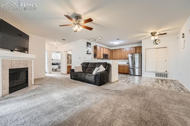living area with a ceiling fan, light colored carpet, a tiled fireplace, visible vents, and rail lighting