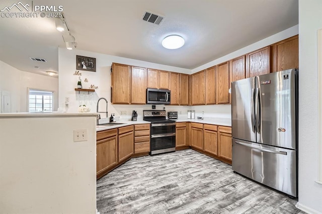 kitchen featuring appliances with stainless steel finishes, brown cabinetry, light wood-style flooring, and visible vents