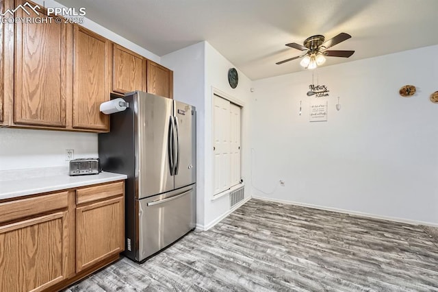 kitchen with brown cabinetry, a ceiling fan, light wood-type flooring, light countertops, and freestanding refrigerator