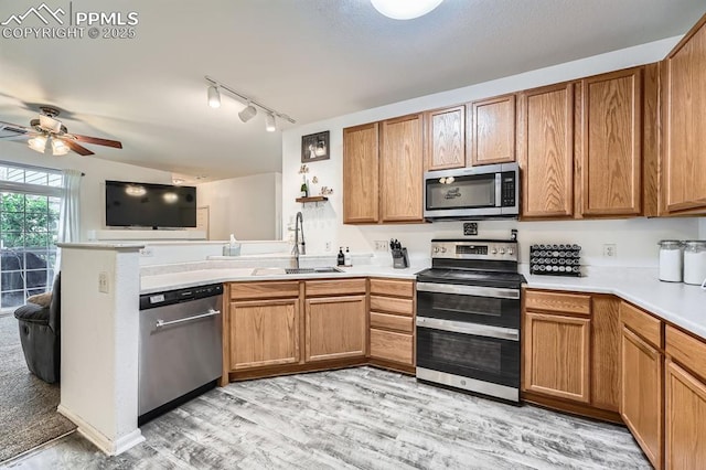 kitchen featuring a sink, a peninsula, light countertops, a ceiling fan, and stainless steel appliances