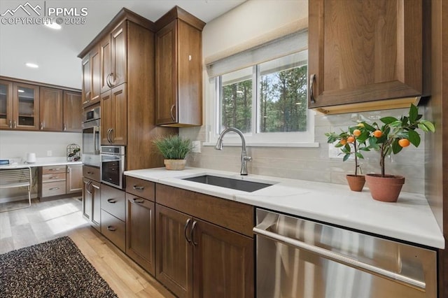 kitchen with backsplash, stainless steel appliances, a sink, and light wood-type flooring