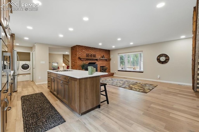 kitchen featuring a kitchen island with sink, a fireplace, open floor plan, washer / clothes dryer, and light wood finished floors