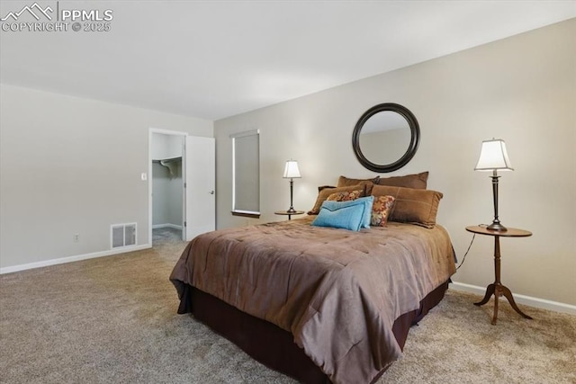 carpeted bedroom featuring visible vents, baseboards, and a walk in closet