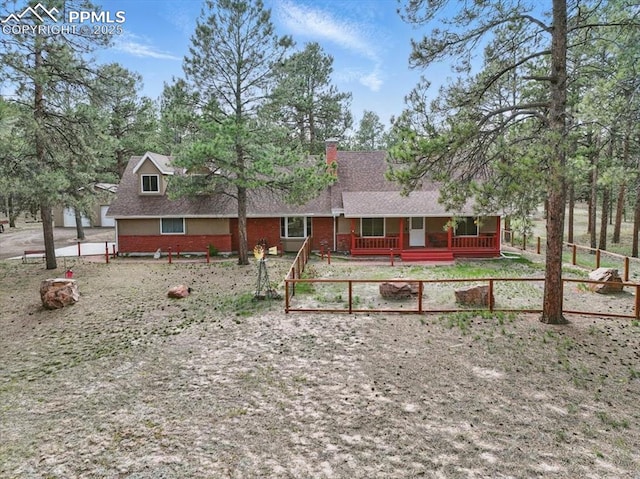 view of front of home with covered porch, a chimney, brick siding, fence, and a shingled roof