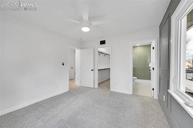 unfurnished bedroom with carpet flooring, a closet, baseboards, ensuite bath, and a walk in closet