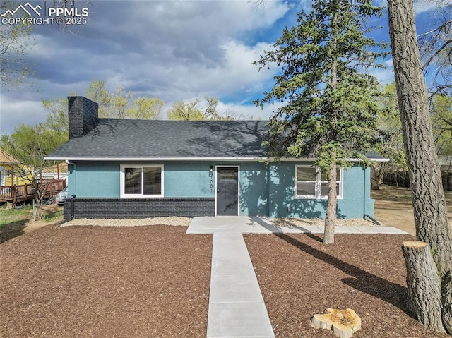 view of front of property featuring a chimney, brick siding, stucco siding, and roof with shingles