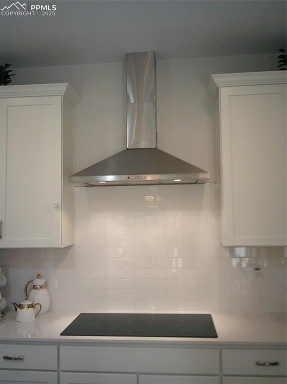 kitchen with white cabinets, backsplash, wall chimney range hood, and light countertops