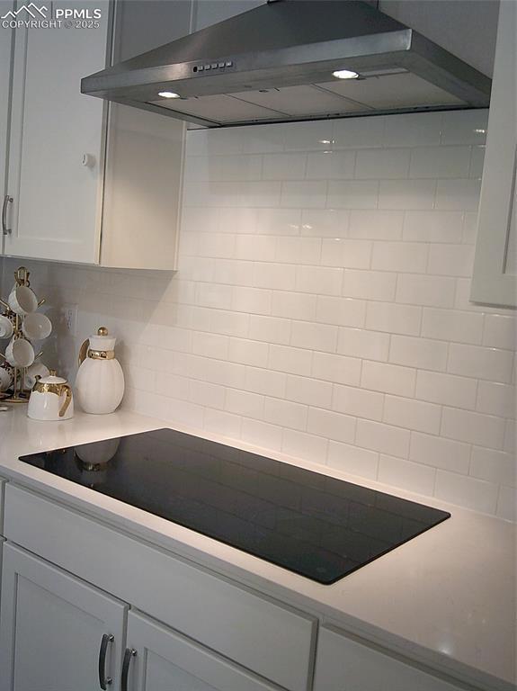 kitchen with under cabinet range hood, black electric cooktop, backsplash, light countertops, and white cabinets