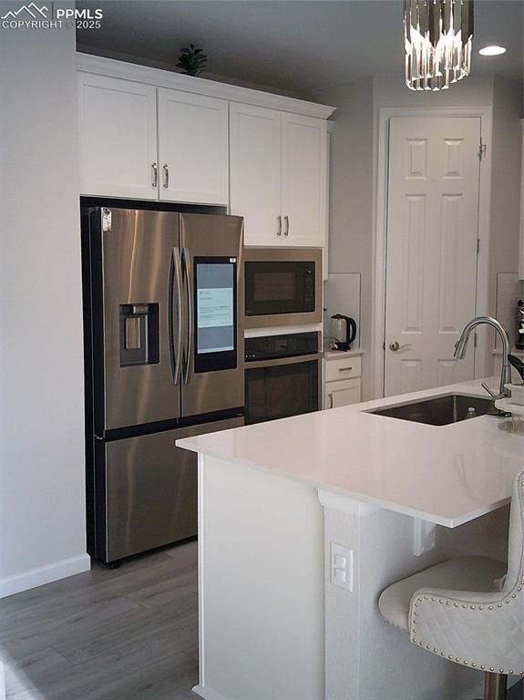 kitchen with black oven, a sink, built in microwave, light wood finished floors, and stainless steel fridge