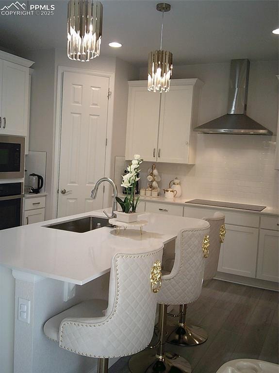 kitchen featuring a chandelier, black electric stovetop, wall chimney exhaust hood, and a sink