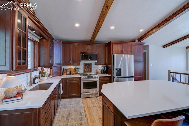 kitchen with light wood-style flooring, backsplash, beamed ceiling, light countertops, and appliances with stainless steel finishes