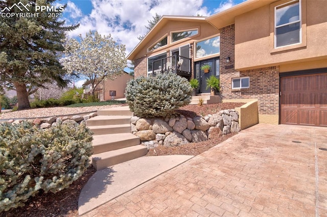 view of home's exterior featuring stucco siding, brick siding, decorative driveway, and a garage