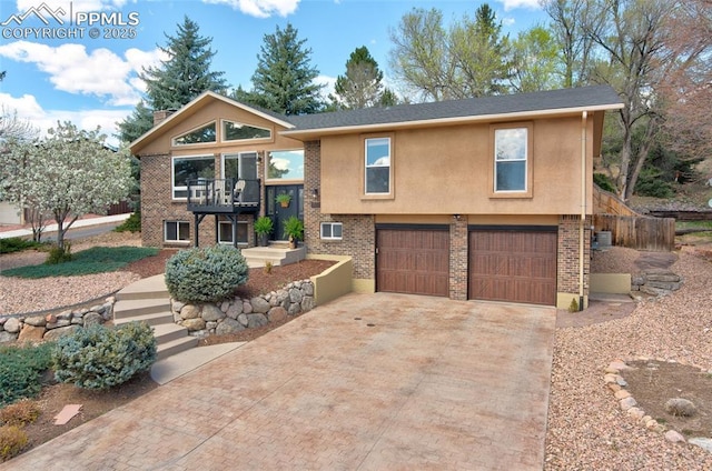 raised ranch with brick siding, an attached garage, a balcony, stucco siding, and decorative driveway