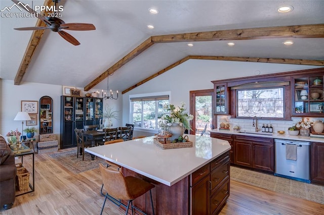kitchen with stainless steel dishwasher, a sink, lofted ceiling with beams, light wood-type flooring, and light countertops