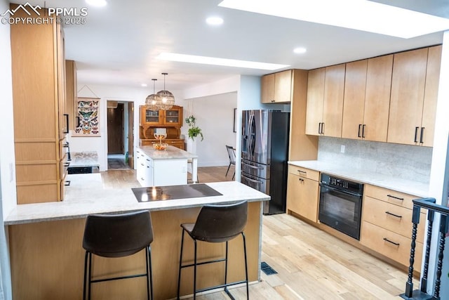 kitchen with backsplash, a peninsula, black appliances, and light brown cabinets