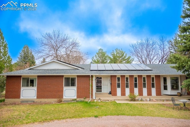 exterior space with a lawn, brick siding, a shingled roof, and roof mounted solar panels