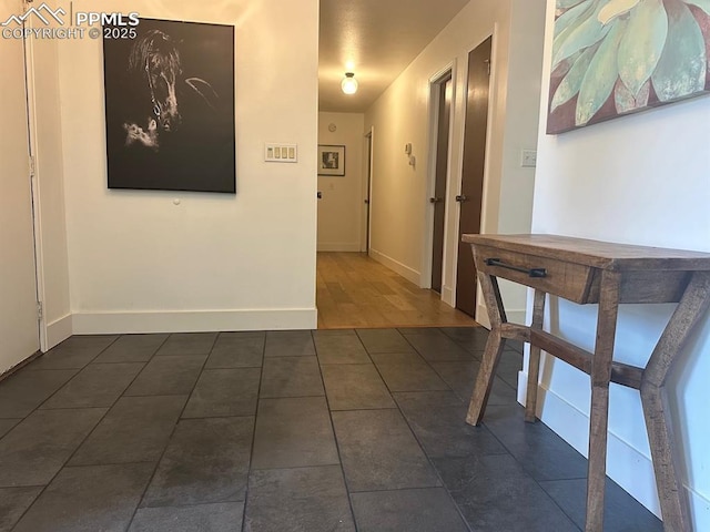 hall featuring dark tile patterned floors and baseboards