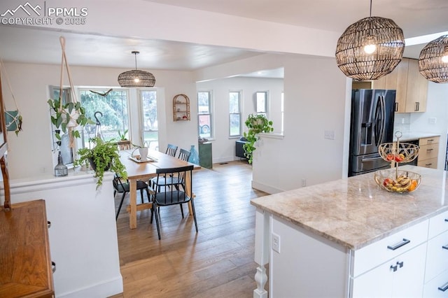 kitchen featuring light wood finished floors, a wealth of natural light, light stone countertops, and fridge with ice dispenser