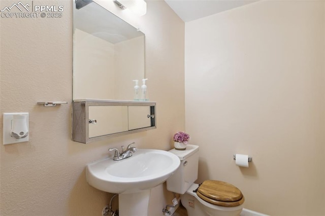 bathroom featuring baseboards, toilet, and a sink