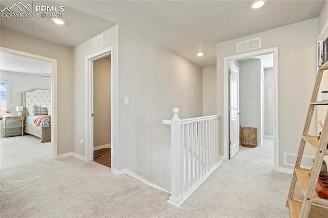 hallway with an upstairs landing, visible vents, and carpet