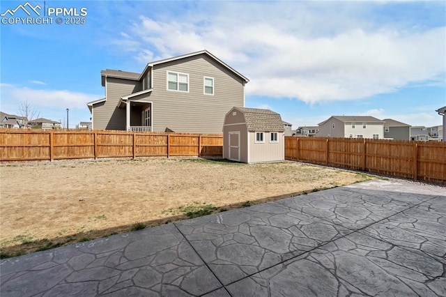 back of property with a fenced backyard, an outdoor structure, a shed, and a patio
