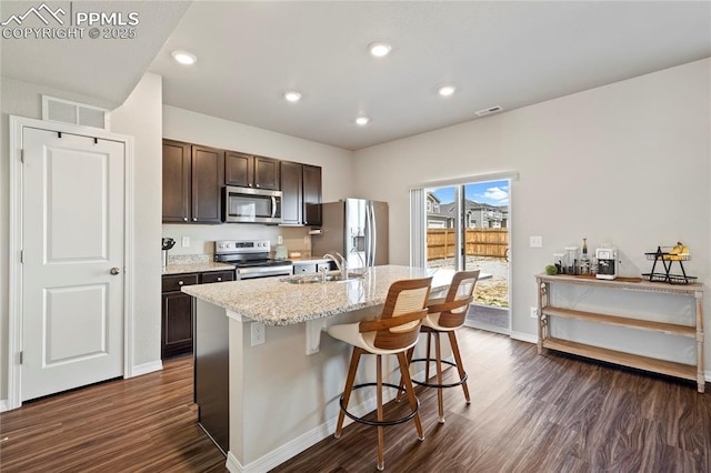 kitchen with stainless steel appliances, a sink, a center island with sink, dark brown cabinets, and dark wood-style flooring