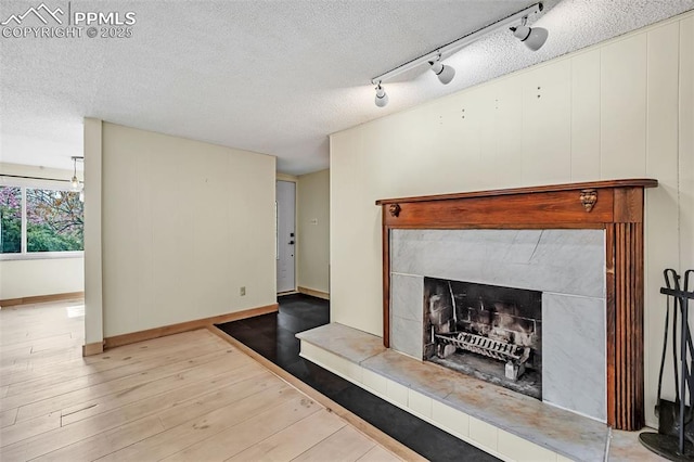1624 Cheyenne Blvd, Colorado Springs, CO 80906 - unfurnished living room with a textured ceiling, a tiled fireplace, wood finished floors, track lighting, and baseboards