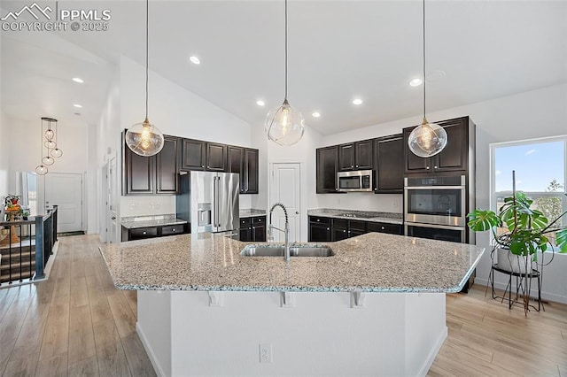 kitchen with light wood finished floors, a sink, stainless steel appliances, a kitchen bar, and a spacious island