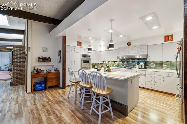 kitchen featuring appliances with stainless steel finishes, light wood-style floors, light countertops, extractor fan, and backsplash