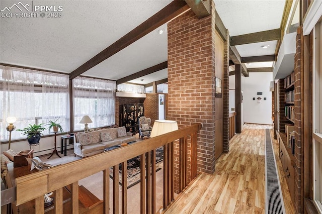 corridor featuring a textured ceiling, brick wall, beam ceiling, and light wood-style floors