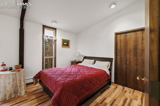 bedroom with a baseboard radiator, wood finished floors, and vaulted ceiling