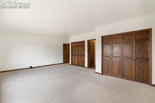 unfurnished bedroom with two closets, baseboards, and light carpet