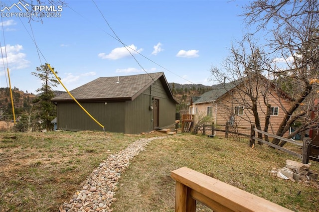 view of home's exterior featuring an outdoor structure, roof with shingles, and fence