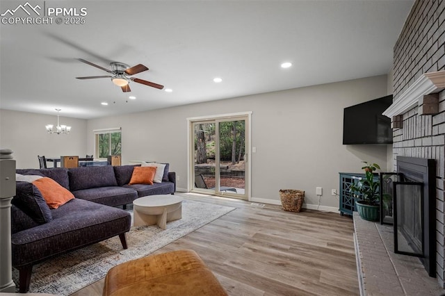 living room with a fireplace, wood finished floors, recessed lighting, and ceiling fan with notable chandelier