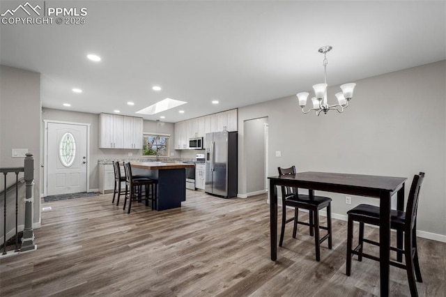 dining room featuring a chandelier, baseboards, recessed lighting, wood finished floors, and a skylight