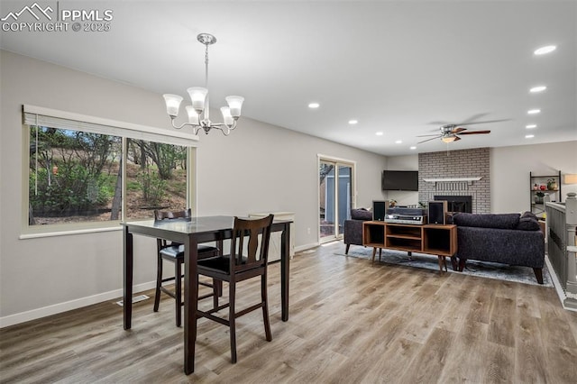 dining room with a fireplace, light wood-type flooring, baseboards, and ceiling fan with notable chandelier