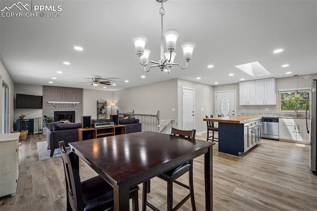 dining space featuring recessed lighting, a skylight, ceiling fan with notable chandelier, and light wood-style flooring