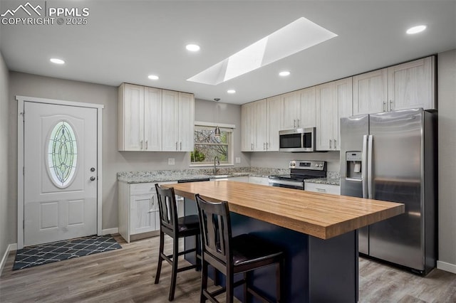 kitchen featuring a sink, butcher block countertops, a kitchen breakfast bar, a skylight, and appliances with stainless steel finishes