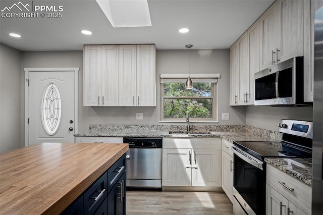 kitchen featuring blue cabinetry, butcher block counters, stainless steel appliances, light wood-style floors, and a sink