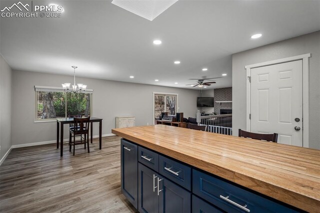 kitchen featuring recessed lighting, butcher block countertops, light wood-style floors, a brick fireplace, and ceiling fan with notable chandelier