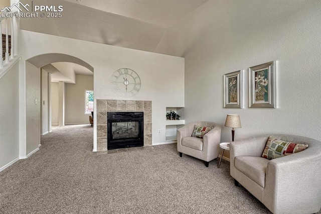 living room with carpet floors, baseboards, a tile fireplace, arched walkways, and vaulted ceiling