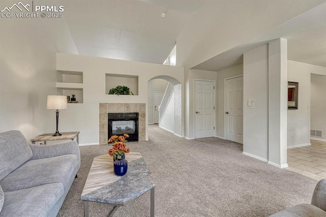 living room with arched walkways, a tile fireplace, carpet, baseboards, and visible vents