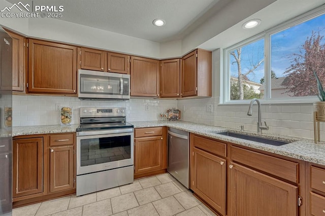 kitchen with a sink, light tile patterned floors, brown cabinetry, backsplash, and appliances with stainless steel finishes