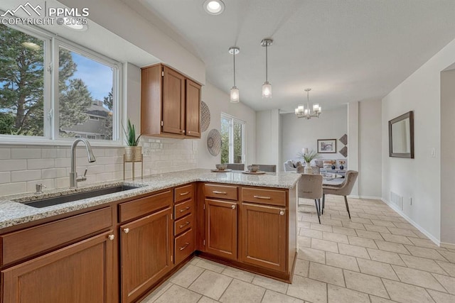 kitchen featuring light stone countertops, brown cabinets, backsplash, a sink, and a peninsula