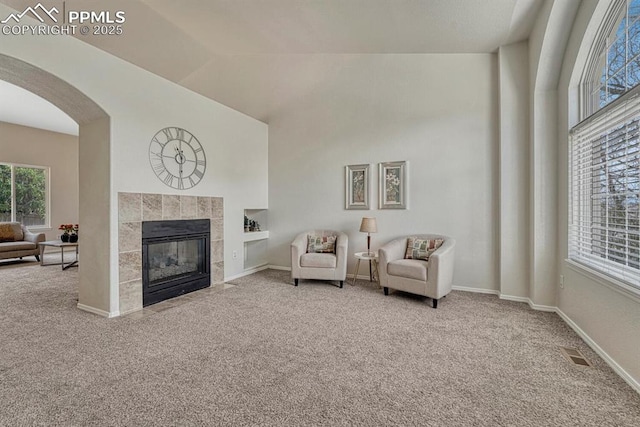 sitting room with carpet, visible vents, a tiled fireplace, and arched walkways