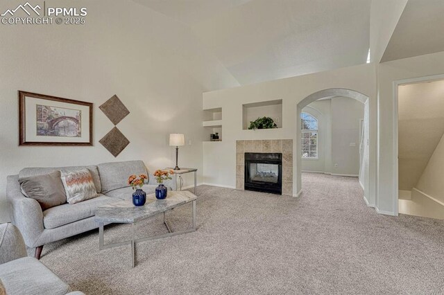 living room with baseboards, arched walkways, vaulted ceiling, a fireplace, and carpet